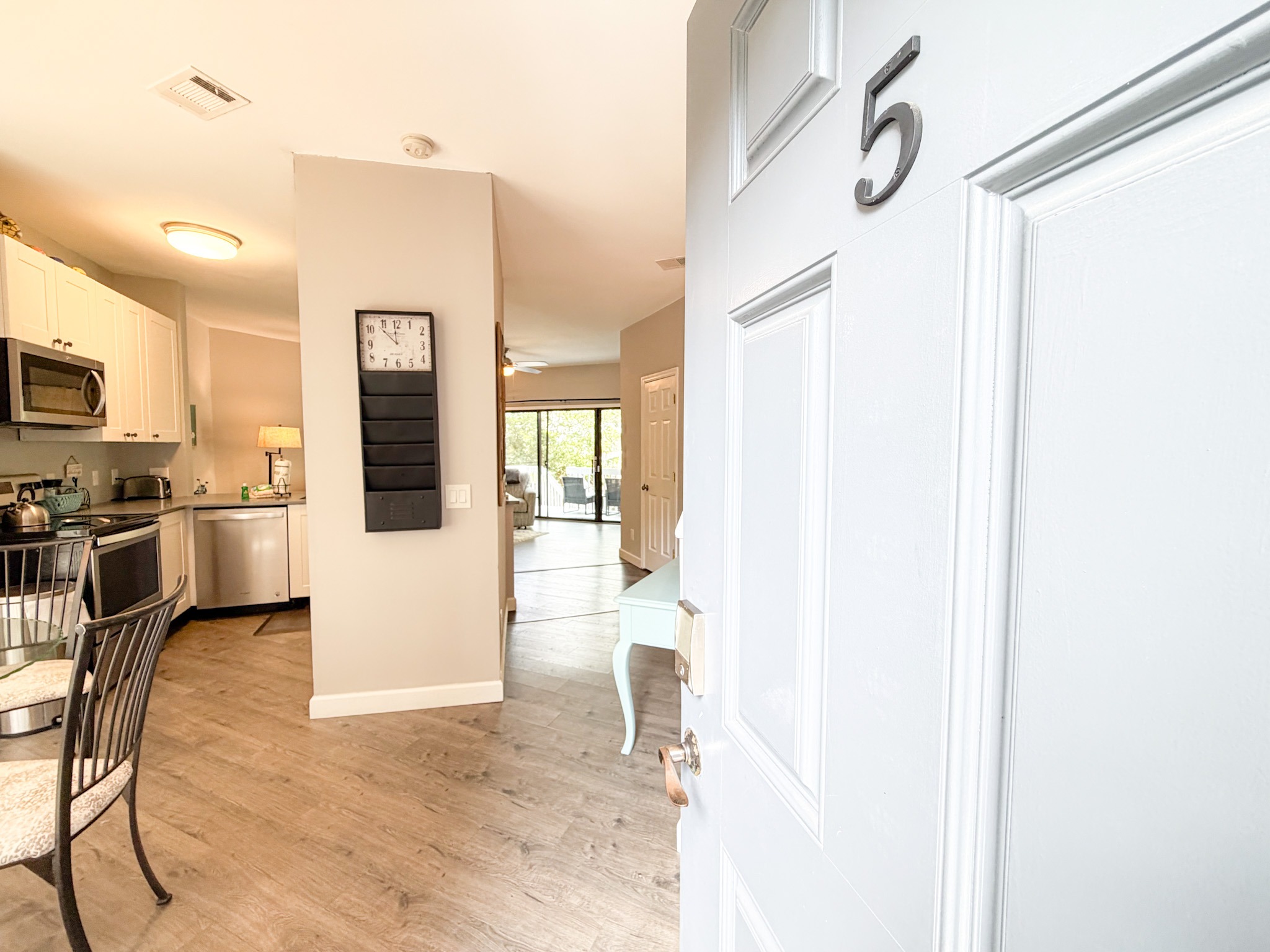 Open pale blue door labeled '5' leads into a bright kitchen and living area with a wall clock and hallway beyond.
